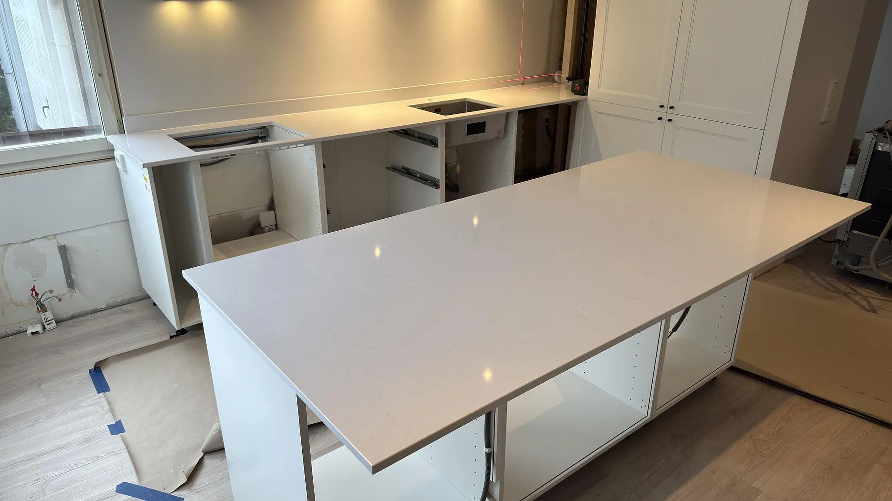 Köksö i polerad vit Technistone Noble Supreme White komposit med separat bänkrad i ett kök under montering i Hammarö.