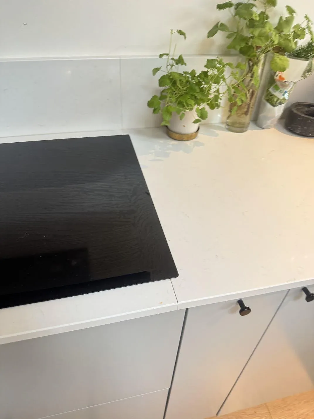 Detalj av polerad Technistone Noble Supreme White komposit vid svart häll och grå köksfronter i Höllviken.