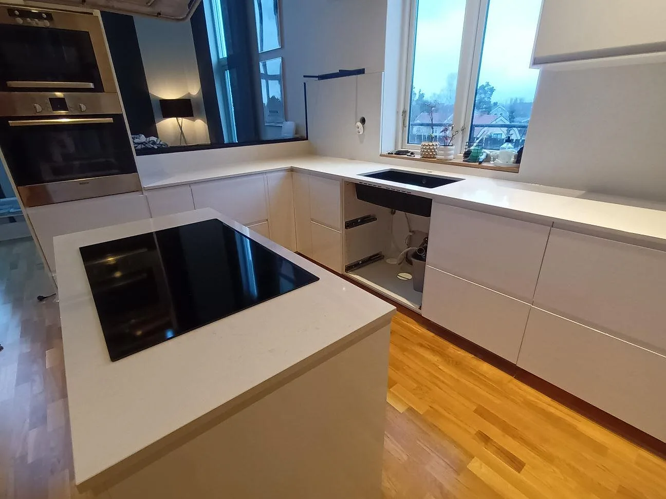 Köksbänkskiva i vit Technistone Noble Supreme White med köksö och induktionshäll samt diskho i bänkraden, tagen under montering i Huddinge.
