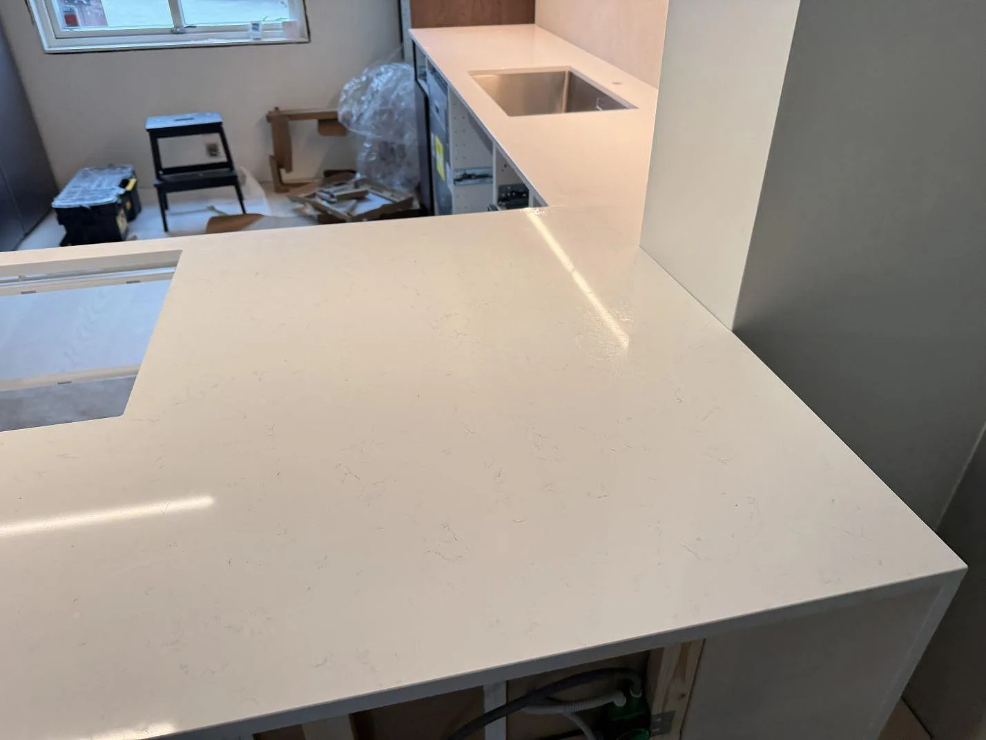 Köksbänkskiva i polerad Technistone Noble Supreme White med ljus ådring och förberedda öppningar under montering i Karlshamn.