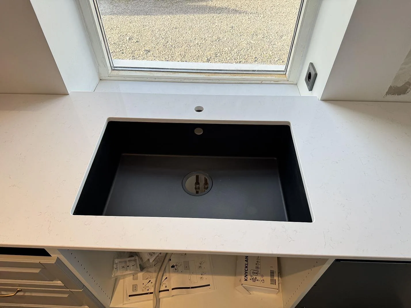 Närbild på polerad köksbänkskiva i Technistone Noble Supreme White med svart diskho och fönsternisch i Klagstorp.