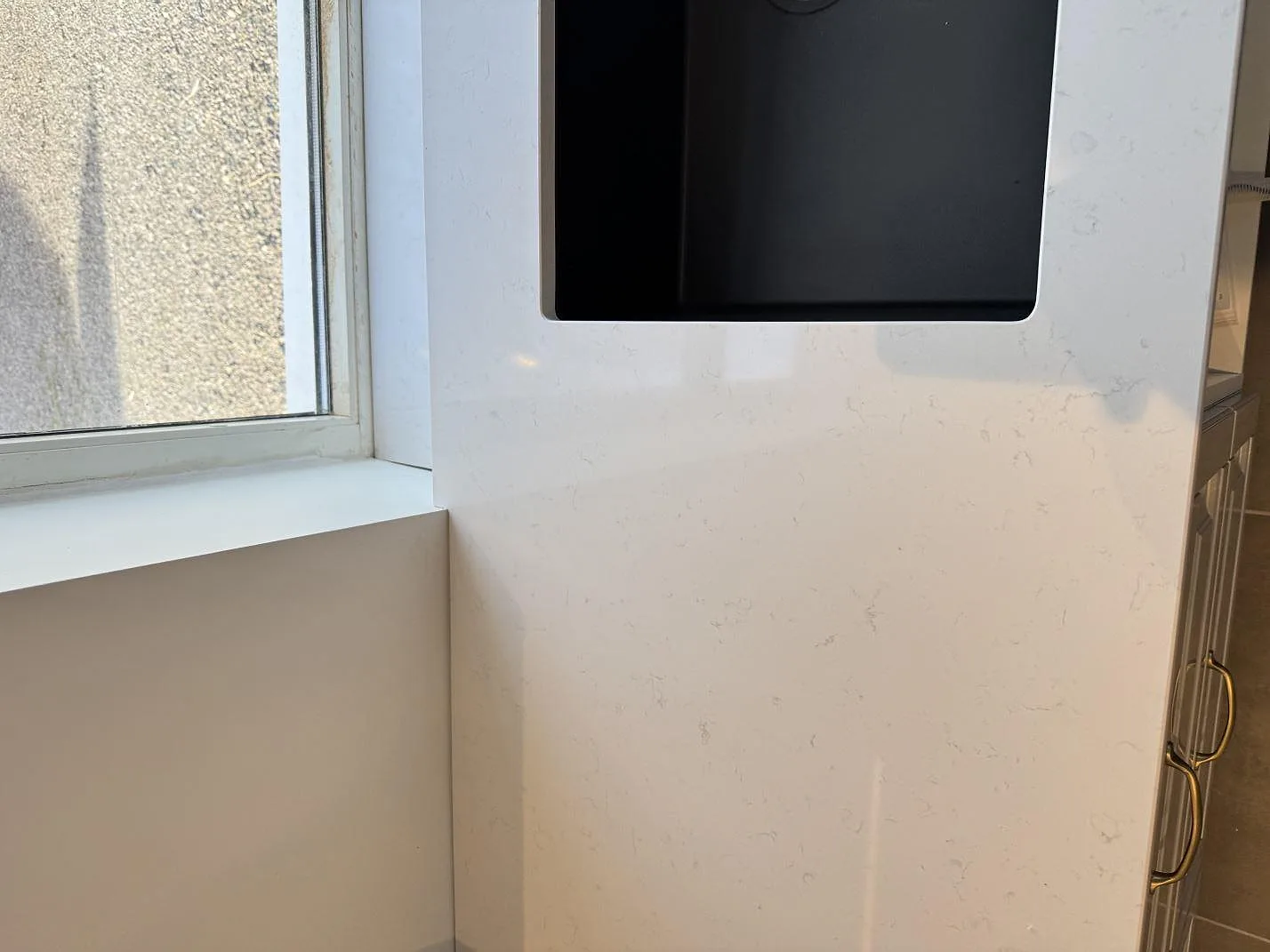 Ytdetalj på vit Technistone Noble Supreme White i polerad komposit intill svart diskho och fönster i Klagstorp.