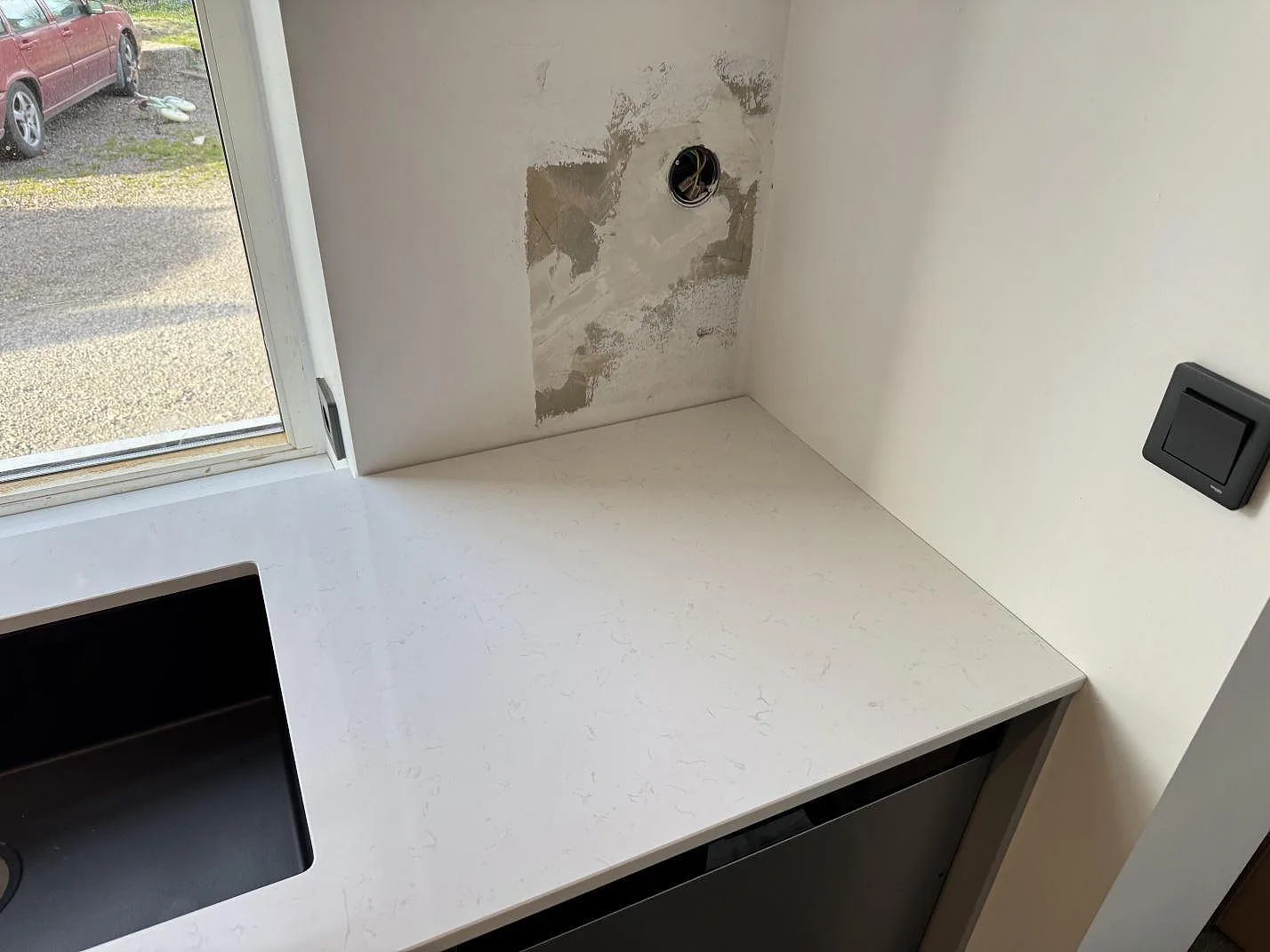 Ljus köksbänkskiva i Technistone Noble Supreme White, polerad kvartskomposit, vid svart diskho och vägg under montering i Klagstorp.