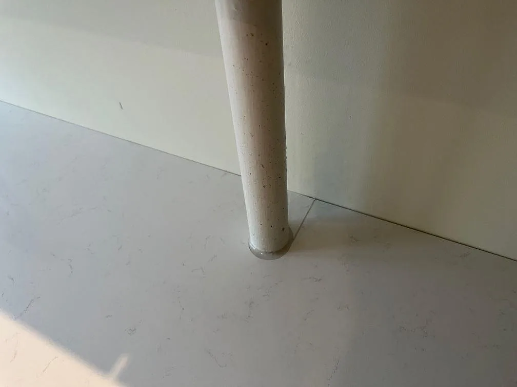 Detalj av ljus kompositbänkskiva i Technistone Noble Supreme White med rörgenomföring vid väggen i København Ø.