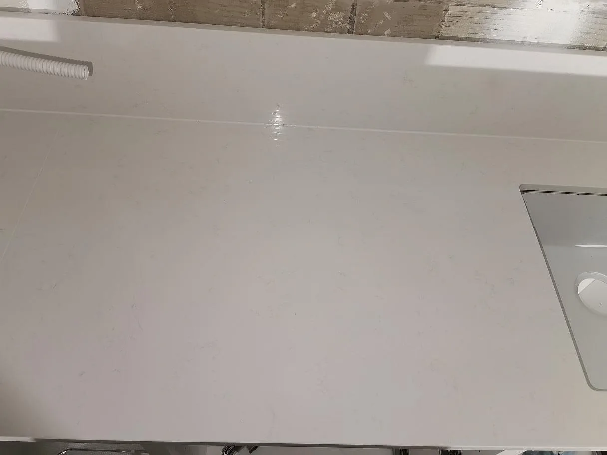Bänkskiva i vit Technistone Noble Supreme White med uppvikt stänkskydd och blandarhål i ett kök i Malmö.