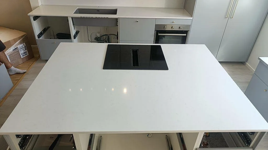 Polerad köksö i vit Technistone Noble Supreme White komposit med nedsänkt induktionshäll och downdraft-fläkt i ett kök i Malmö.
