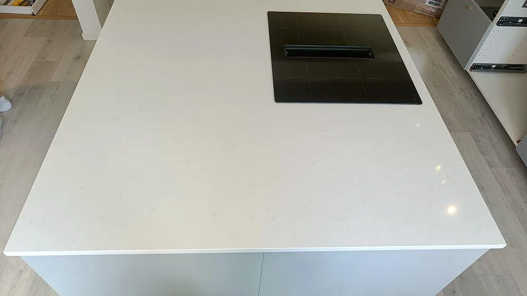 Ovanifrån av polerad köksö i vit Technistone Noble Supreme White komposit med induktionshäll i ett kök i Malmö.