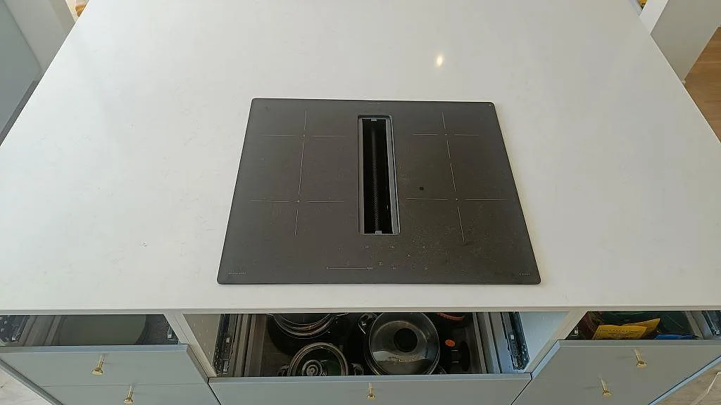 Närbild på induktionshäll med integrerad fläkt nedsänkt i vit Technistone Noble Supreme White kompositbänk i Malmö.