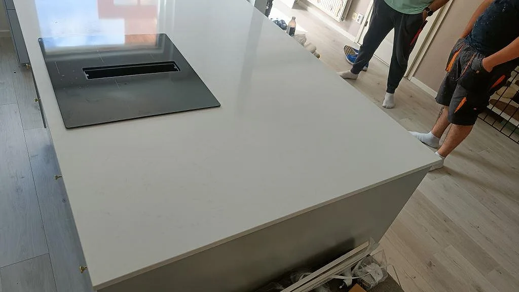 Vit kompositbänkskiva i Technistone Noble Supreme White med induktionshäll på köksön, sedd i köksmiljö i Malmö.