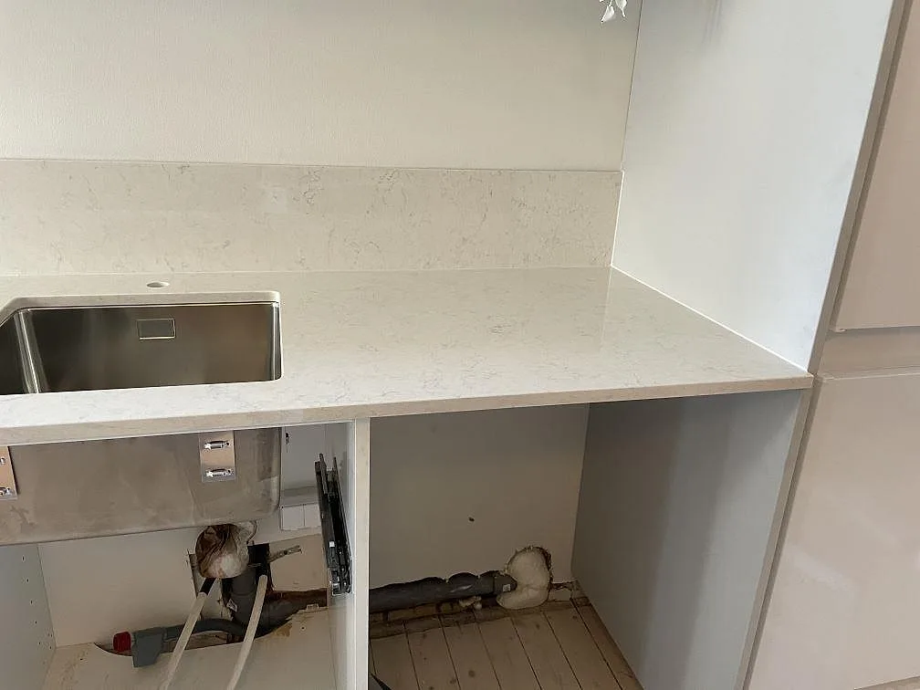 Köksbänkskiva i vit Technistone Noble Supreme White, polerad komposit, med rostfri diskho och uppvikt stänkkant under montering i Malmö.