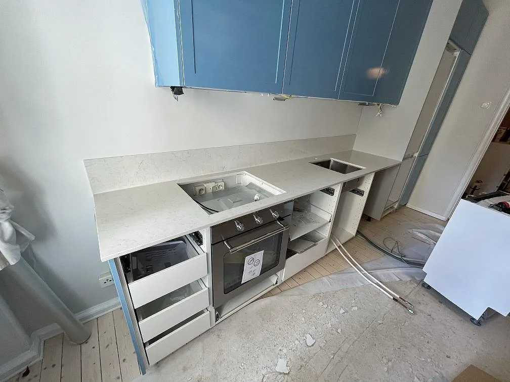 Köksbänkskiva i vit Technistone Noble Supreme White, polerad komposit, med blå skåp, hällöppning och rostfri diskho i Malmö.