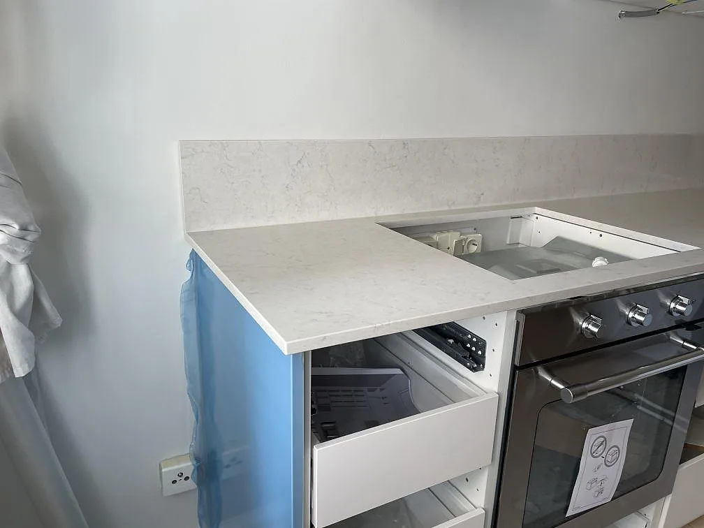 L-formad köksbänkskiva i Technistone Noble Supreme White, polerad kvartskomposit, med uppvikt stänkkant och hällöppning i Malmö.