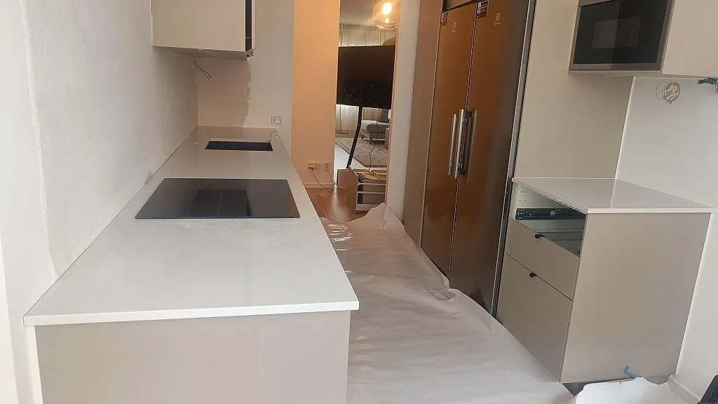 Köksbänkskiva i vit Technistone Noble Supreme White, polerad, med svart häll och separat bänkdel under montering i Malmö.