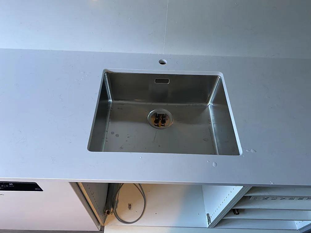 Närbild på rostfri diskho i polerad Technistone Noble Supreme White med ljus komposityta och stänkskydd i Malmö.