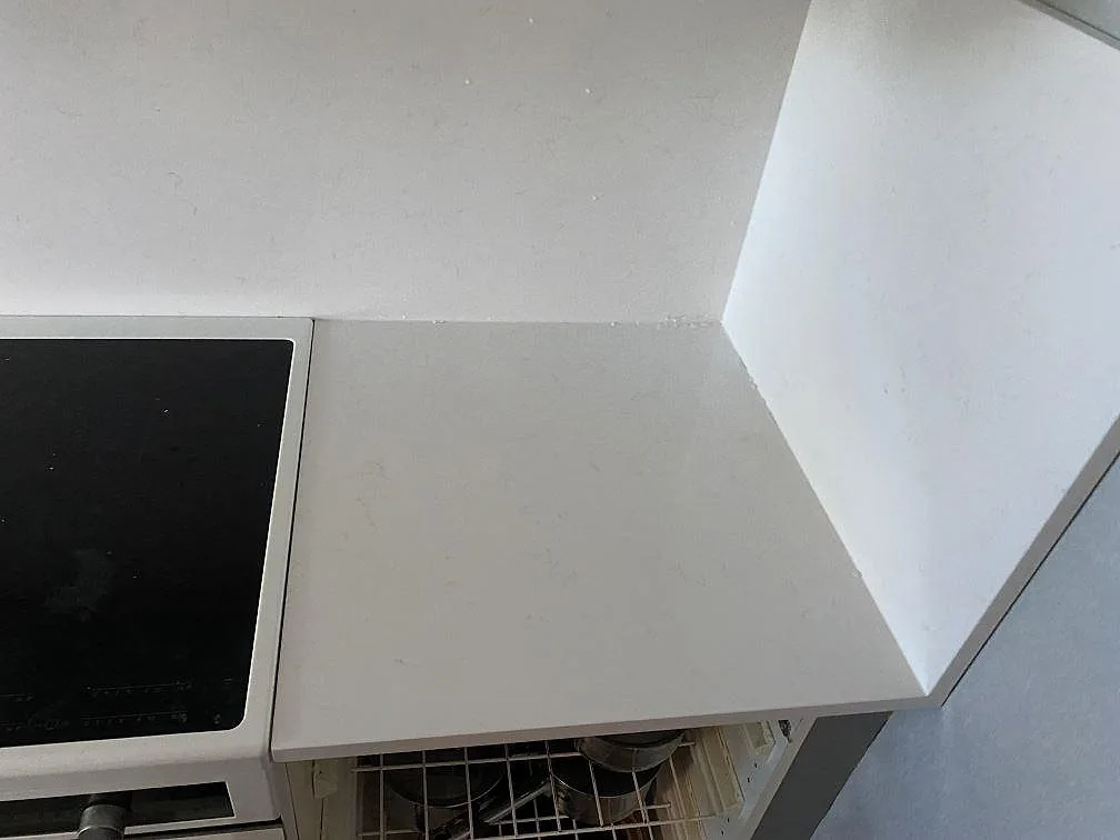 Hörndetalj vid spis i polerad Technistone Noble Supreme White, vit kompositbänkskiva med stänkskydd i Malmö.