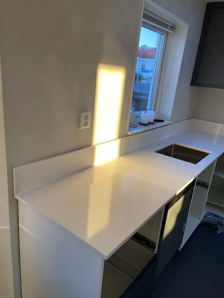 Köksö i vit Technistone Noble Supreme White med utskuren plats för häll i ett kök under montering i Mörarp.