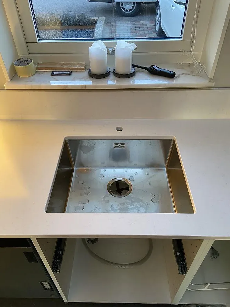 Underlimmad rostfri diskho i en köksö av vit Technistone Noble Supreme White vid fönstret i ett kök i Mörarp.