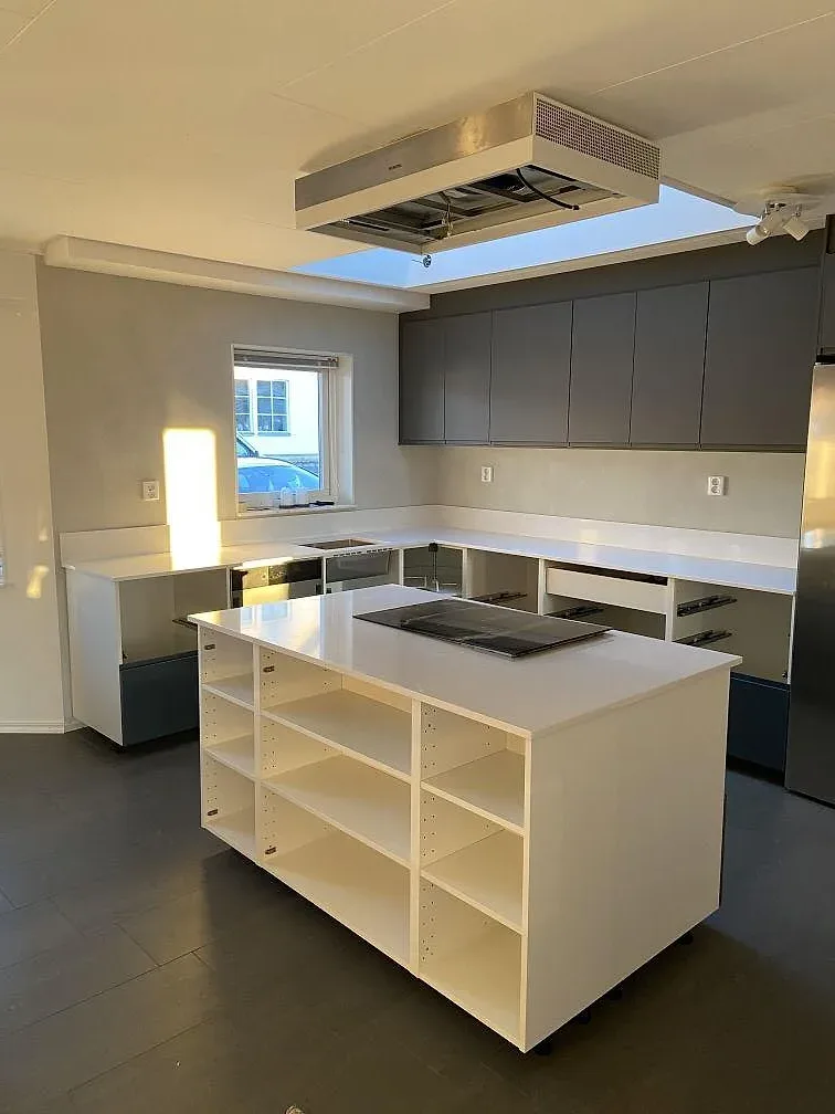 Vit Technistone Noble Supreme White som köksö och bänkskiva i ett ljust kök under montering med marinbla skåp och köksfläkt i Mörarp.