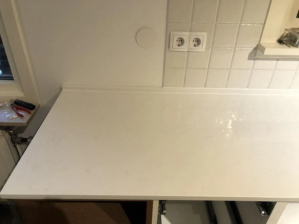 Vit kvartskompositbänk i Technistone Noble Supreme White mot vitt kakel och eluttag i ett kök under inredning i Sävedalen.