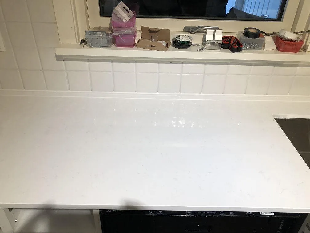 Polerad vit köksbänkskiva i Technistone Noble Supreme White med glänsande yta och vitt kakel som stänkskydd i ett kök i Sävedalen.