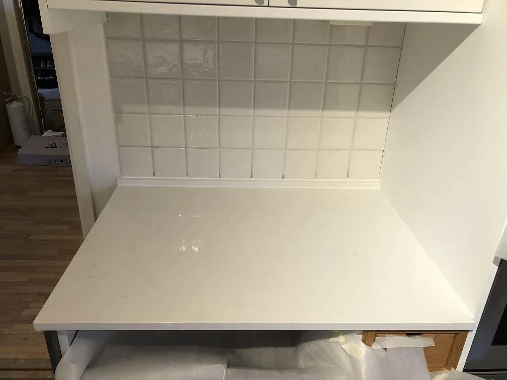 Polerad vit köksbänkskiva i Technistone Noble Supreme White mot ljust kakel i ett kök under montering i Sävedalen.