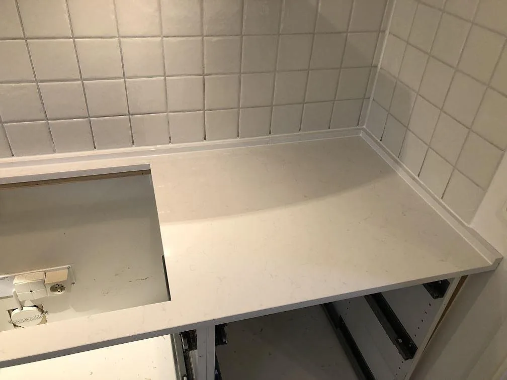Hörnparti av vit polerad köksbänkskiva i Technistone Noble Supreme White mot vitt kakel i ett kök i Sävedalen.