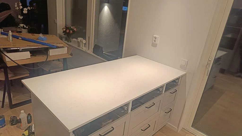Köksö i vit Technistone Noble Supreme White komposit med slät kant och öppna lådstommar i ett kök i Skegrie.