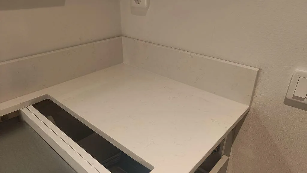 Hörndetalj av vit Technistone Noble Supreme White bänkskiva med uppvikt stänkkant i ett kök i Skegrie.