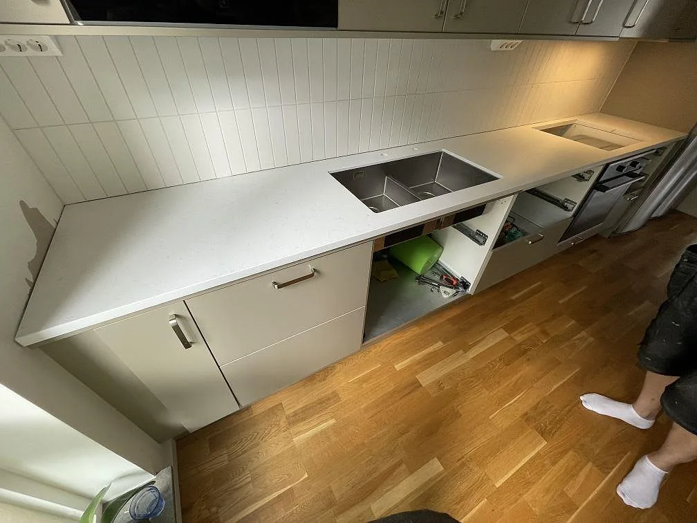 Lång köksbänk i polerad Technistone Noble Supreme White med rostfri diskho, kaklad vägg och ljus inredning i Stockholm.