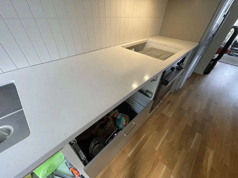 Detalj av polerad köksbänkskiva i Technistone Noble Supreme White med hällöppning, diskho i kanten och ljus grå ådring i Stockholm.