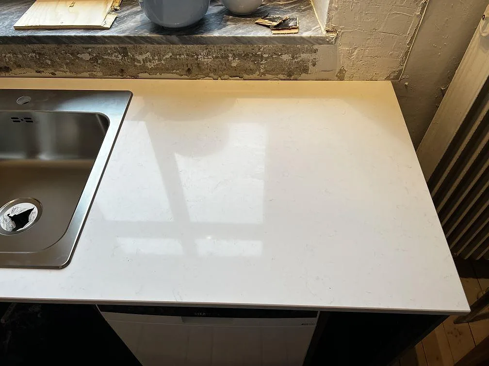Detalj av polerad vit kompositbänkskiva i Technistone Noble Supreme White vid rostfri diskho och rå stänkyta i Trelleborg.