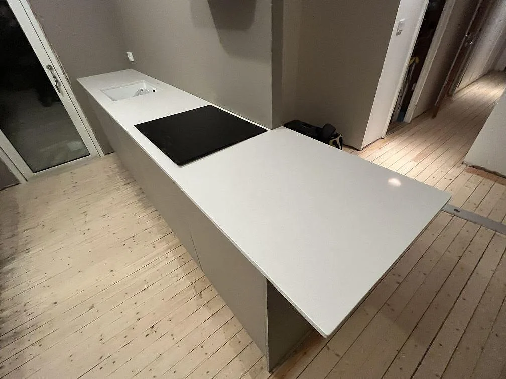 Polerad köksbänkskiva i Technistone Noble Supreme White med svart induktionshäll på en peninsula i ett kök i Trosa.