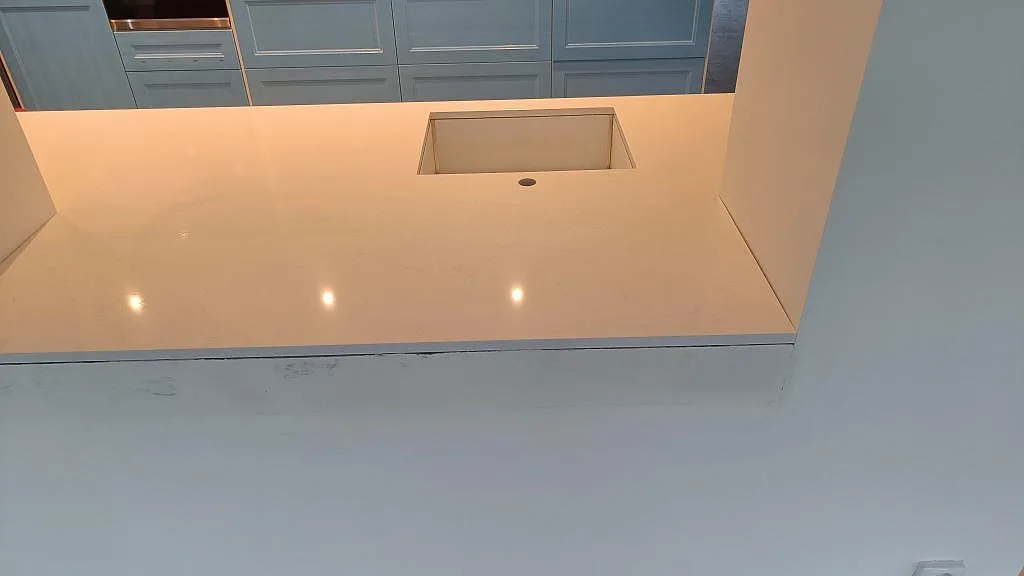 Polerad köksbänkskiva i vit Technistone Noble Supreme White med diskhourtag och reflekterande spotlights i ett kök i Tygelsjö.