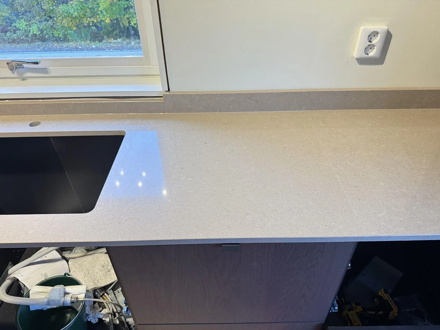 Rak bänkrad i polerad Technistone Noble Troya-komposit med urtag för diskho och stänkkant framför fönster i Hällingsjö.