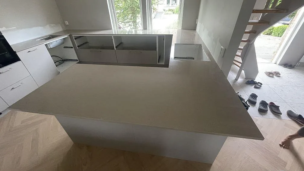 Översikt av kök under montering i Höllviken med polerad Technistone Noble Troya kvartskomposit på central bänkyta och väggbänkar.