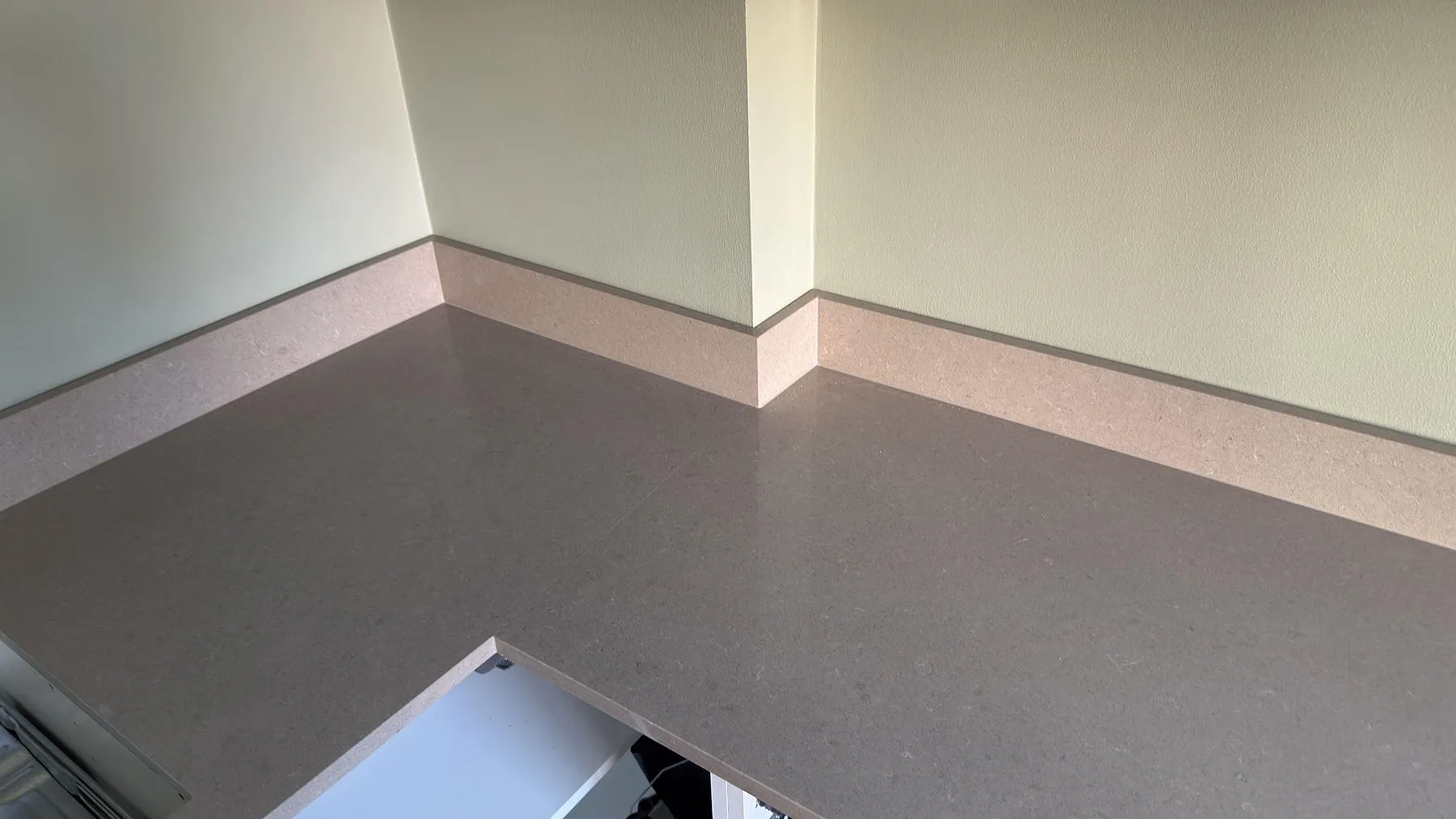 Ytdetalj av polerad Technistone Noble Troya komposit med fin gråbeige kornighet och stänkkant längs väggen i ett kök i Huddinge.