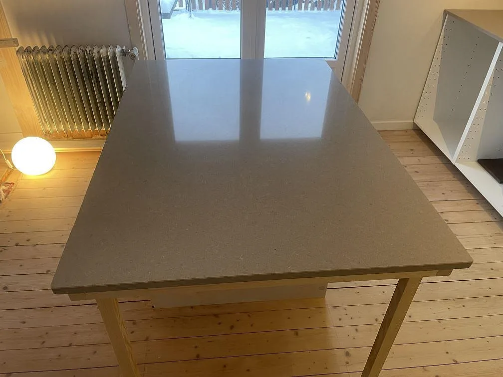 Köksö i Technistone Noble Troya komposit med polerad, spegelblank yta som reflekterar fönstret, i ett kök under montering i Karlstad.