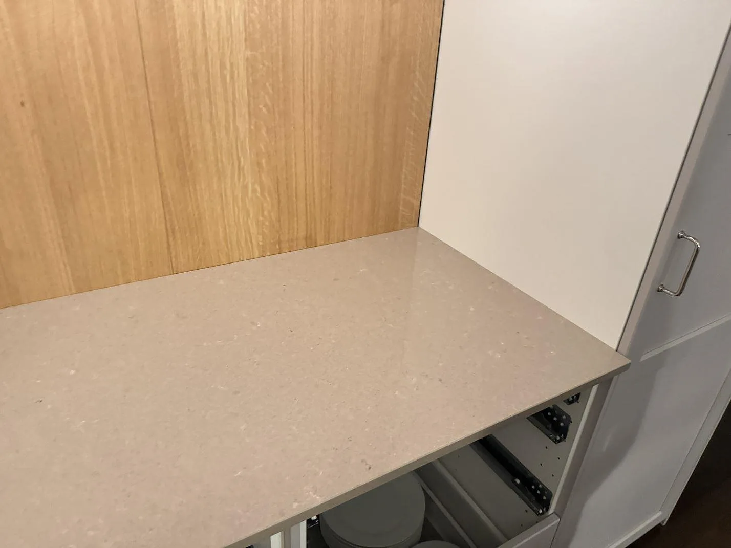 Hörnsektion av köksbänkskiva i polerad Technistone Noble Troya mot träpanel och vit skåpsida i Löddeköpinge.