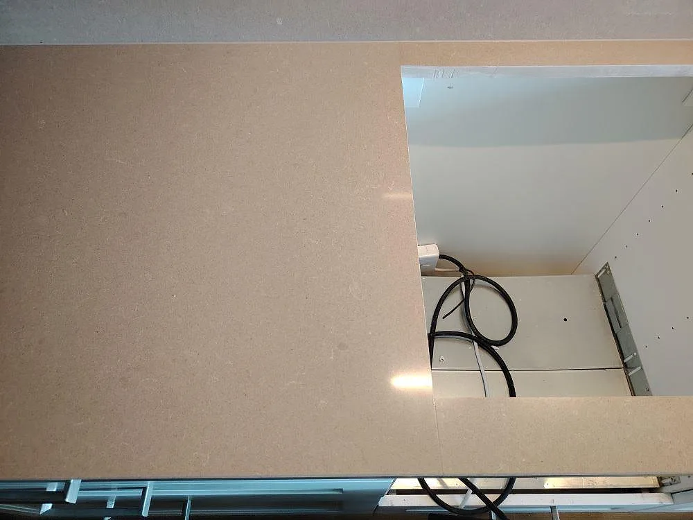 Detalj av polerad Technistone Noble Troya komposit med rektangulärt urtag och synliga monteringskablar i köket i Stockholm.