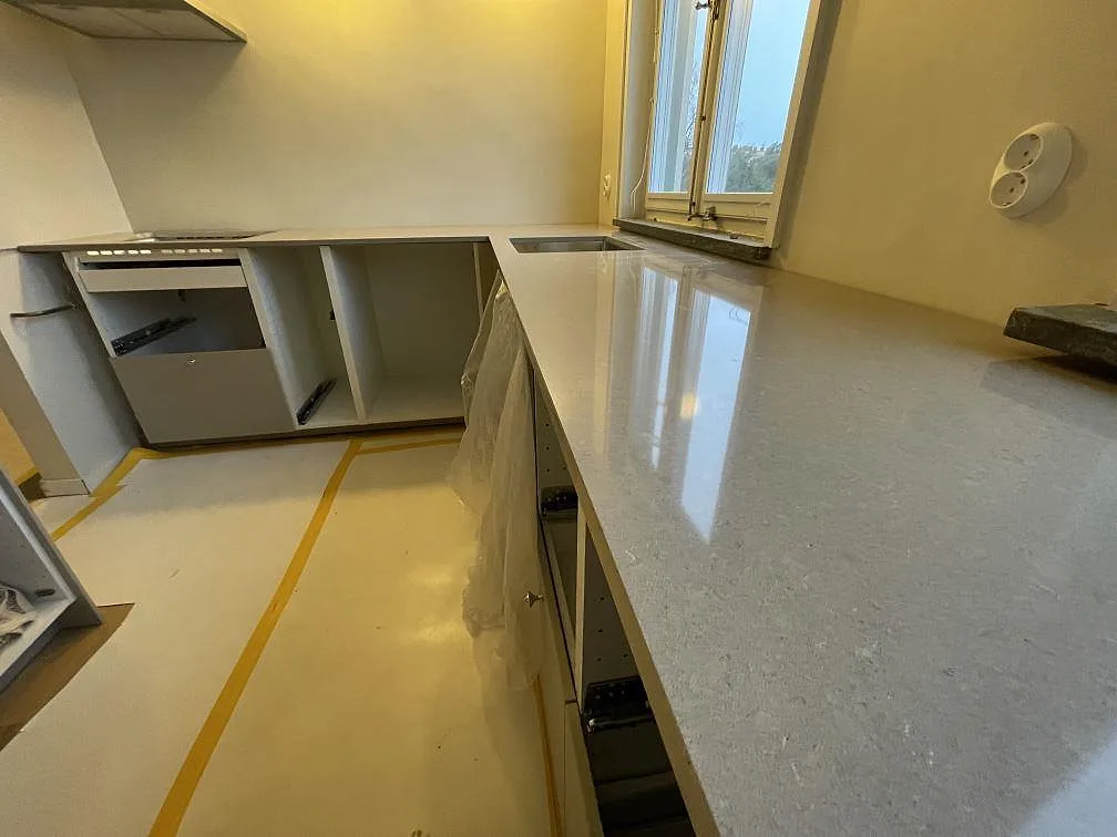 Närbild längs en polerad bänkskiva i Technistone Noble Troya med fin grå ådring, diskhozon och fönster i ett kök i Stockholm.