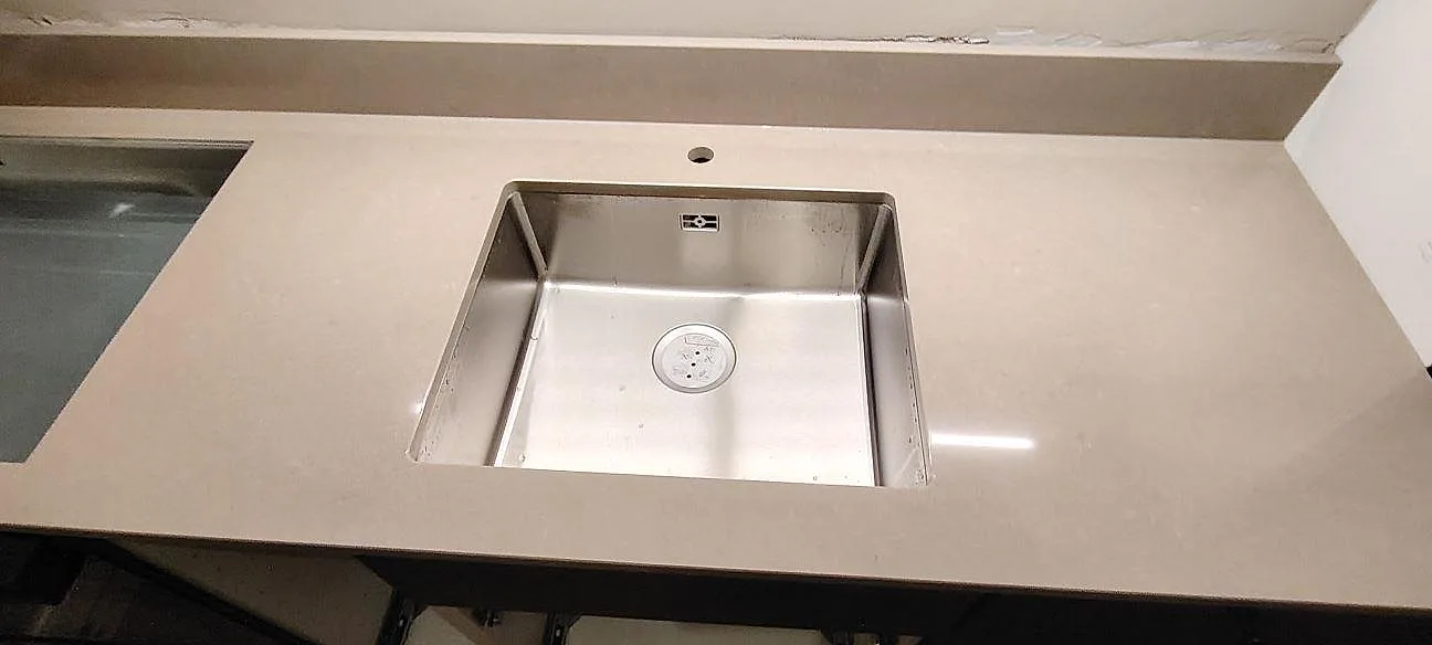 Närbild på rostfri diskho i polerad Technistone Noble Troya med ljus gråbeige kvartskomposit och låg stänkkant i Sundbyberg.