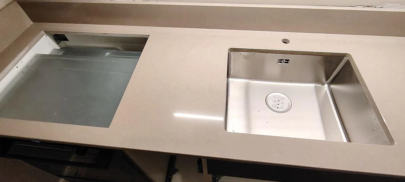 Topvy av polerad Technistone Noble Troya-bänkskiva med rostfri diskho, förberedd hällplats och stänkkant i ett kök i Sundbyberg.
