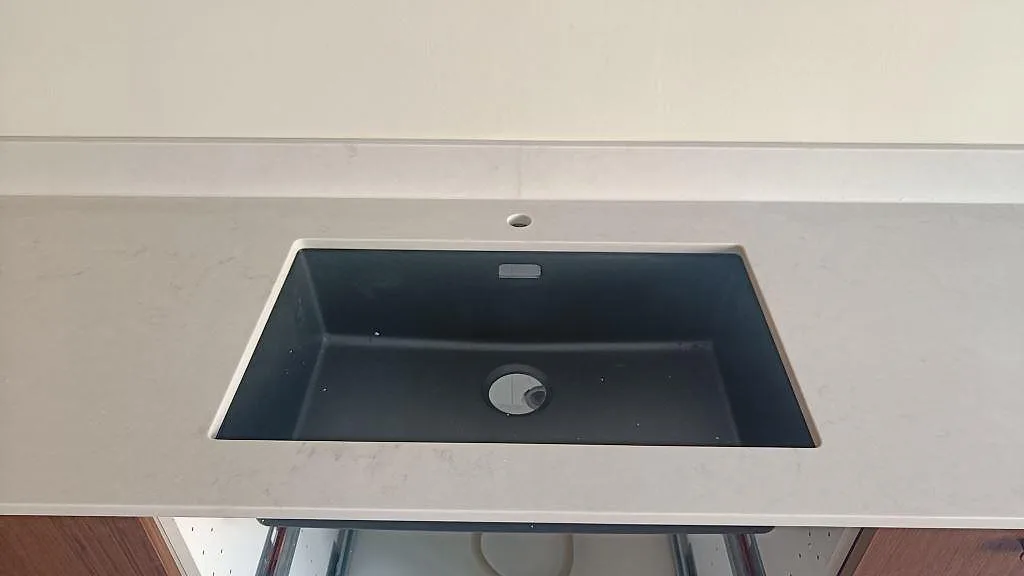 Närbild av svart diskho i en ljus köksbänkskiva av matt Technistone Noble Villa i Göteborg.