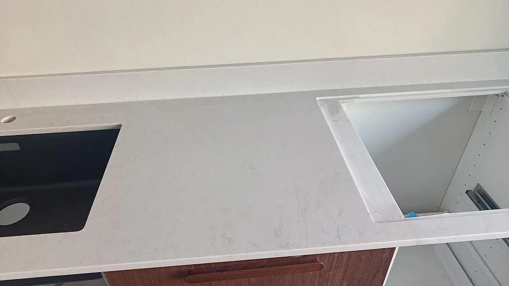 Detalj av bänkskiva i matt Technistone Noble Villa med diskho och öppet skåputrymme under montering i Göteborg.