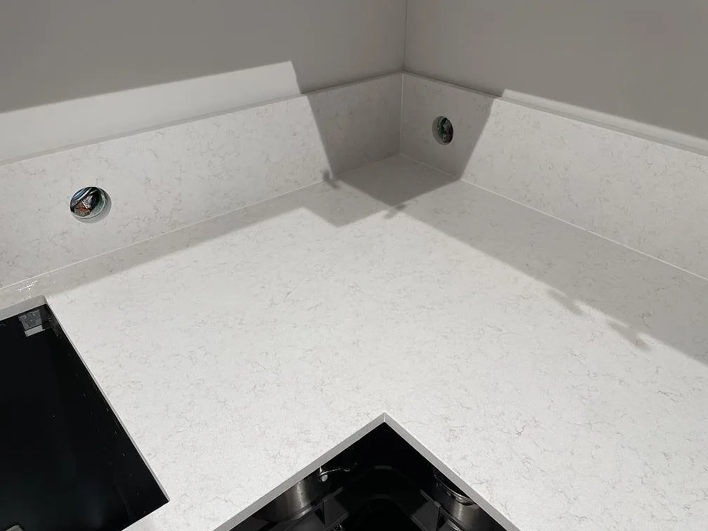 Inre hörn av bänkskivan i Technistone Noble Vintage med uppvikt stänkkant och infällda spotlights, som visar den mjuka grå ådringen, i ett kök i Hägersten.