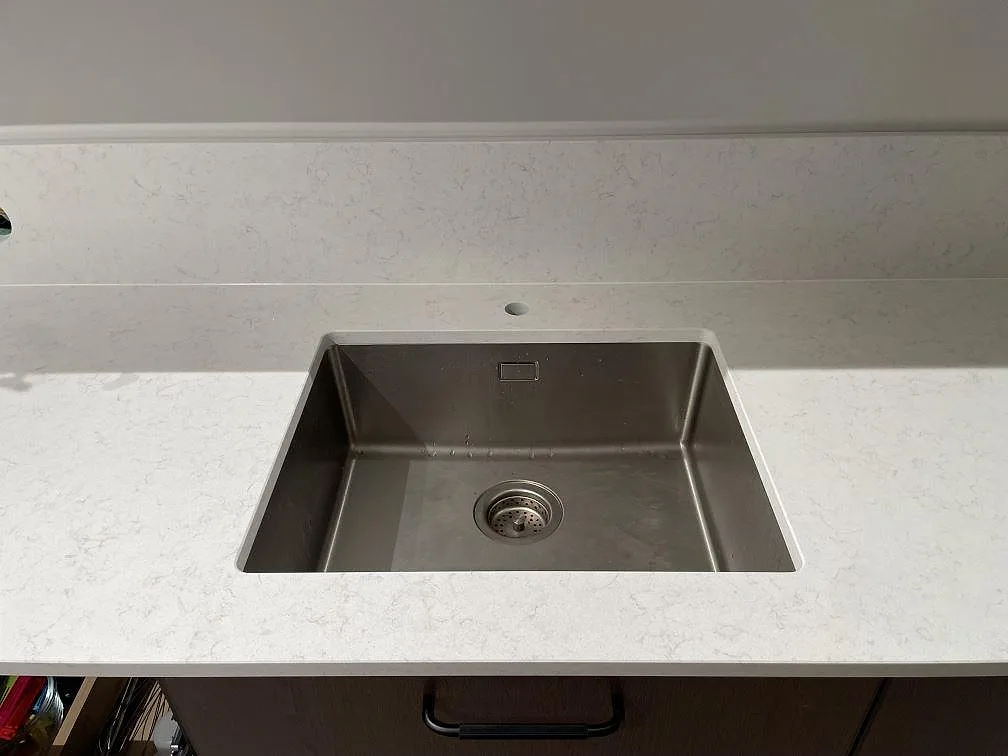 Underlimmad rostfri diskho i en köksbänkskiva i matt Technistone Noble Vintage, med uppvikt stänkkant bakom, i ett kök i Hägersten.