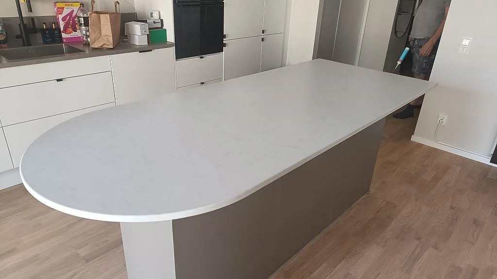 Köksö i 20 mm matt Technistone Noble Vintage komposit med rundad ände och köksinredning bakom i Hovås.