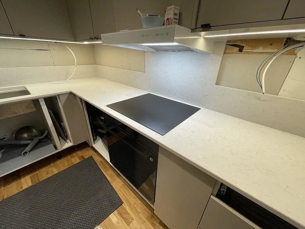 Bänkrad i matt Technistone Noble Vintage med infälld induktionshäll och frihängande köksfläkt i ett kök i Stockholm.