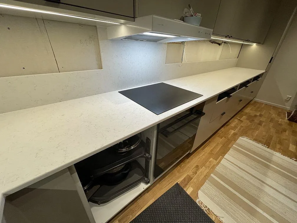 Infälld induktionshäll i en lång bänkskiva av matt vit Technistone Noble Vintage med grå ådring i ett kök i Stockholm.