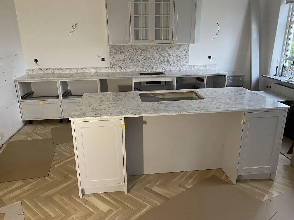 Köksbänkskiva i polerad Technistone Romano Ricco, vitgrå komposit, med köksö och stänkskydd i ett kök i Bjärred.